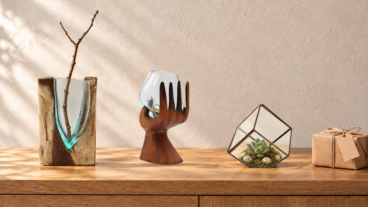 V-shaped molten glass vase with a bare branch, a glass bowl in a carved wooden hand holding keys and a cube terrarium with a succulent on an oak sideboard