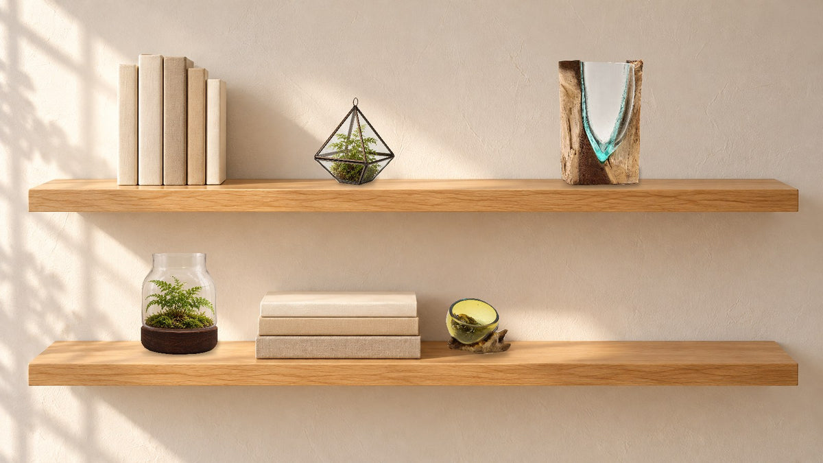 Two oak floating shelves styled with plain books, a small diamond terrarium with a fern, a V-shaped glass vase, a medium terrarium with a fern and a mini amber glass bowl, a third of each shelf left empty