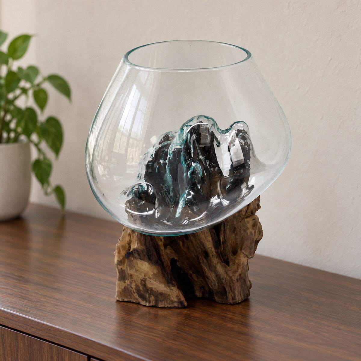 Large molten glass bowl on a wood stump, empty, on a walnut sideboard beside a potted plant
