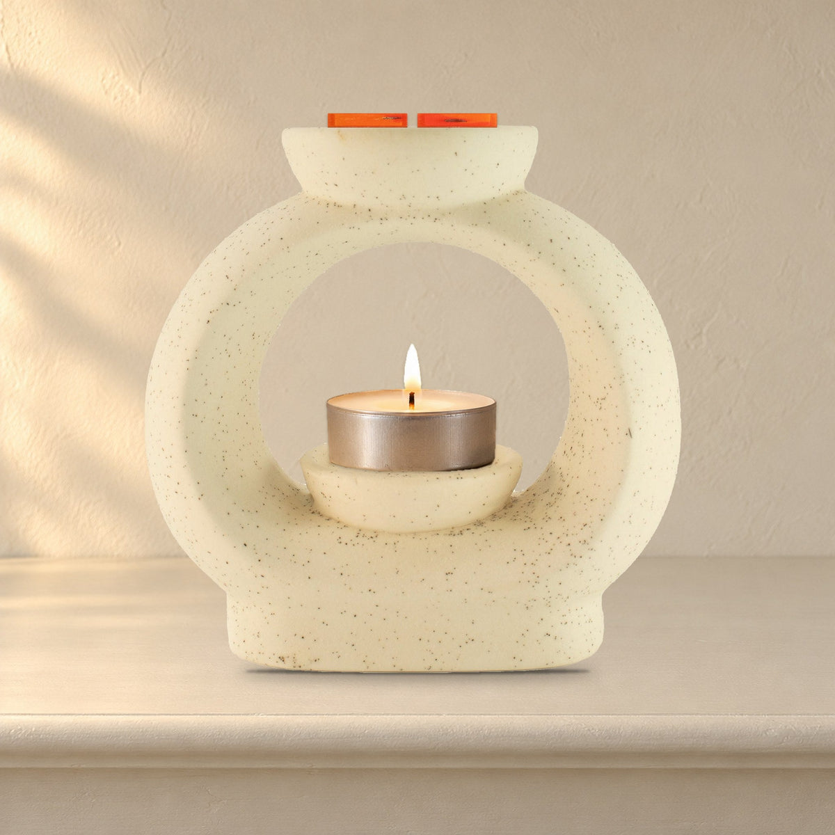 Large speckled off-white pebble wax burner with a lit tealight and Carnelian Fire wax melt squares, on a painted mantelpiece