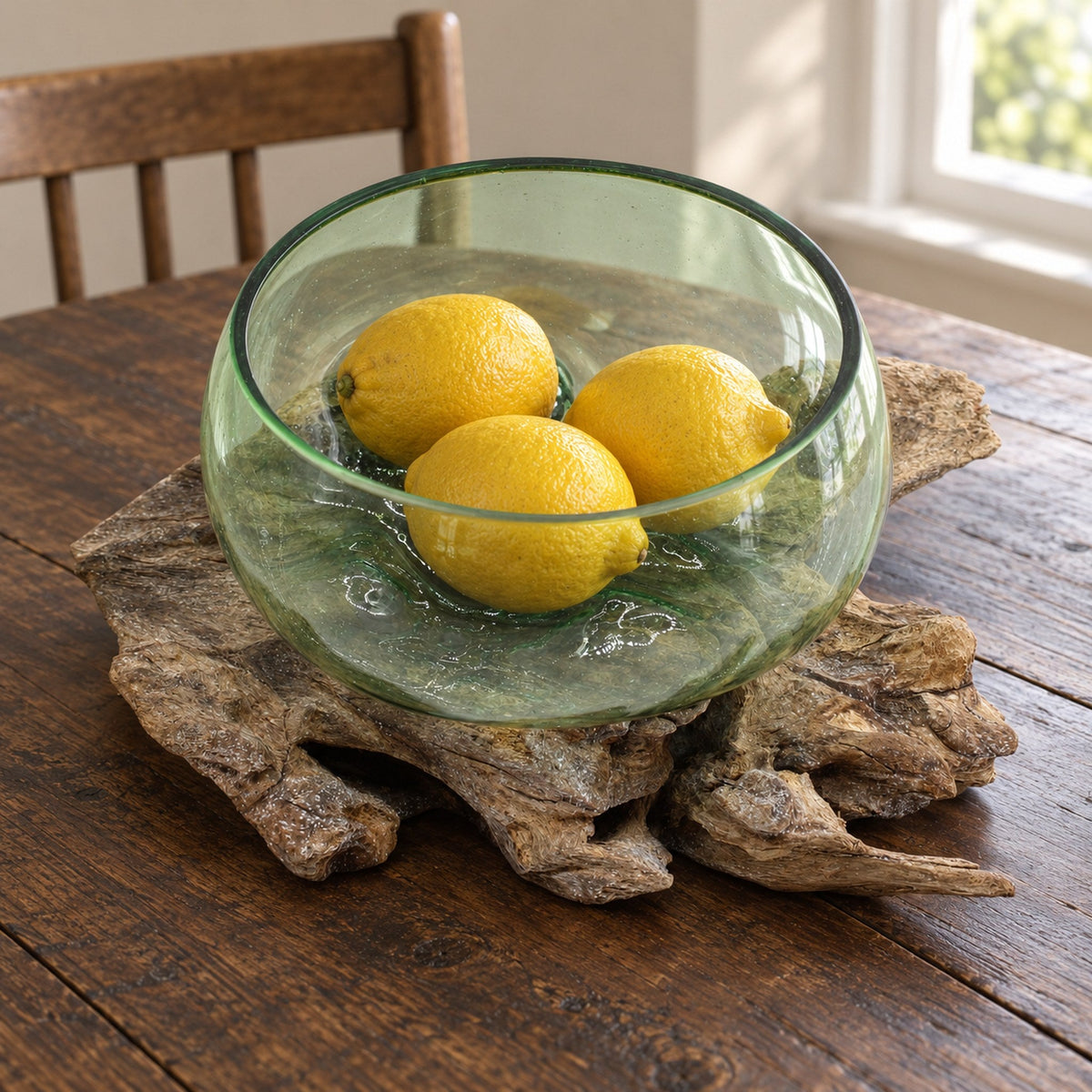 Large wide beer bottle glass bowl on wood holding three whole lemons, on a farmhouse dining table
