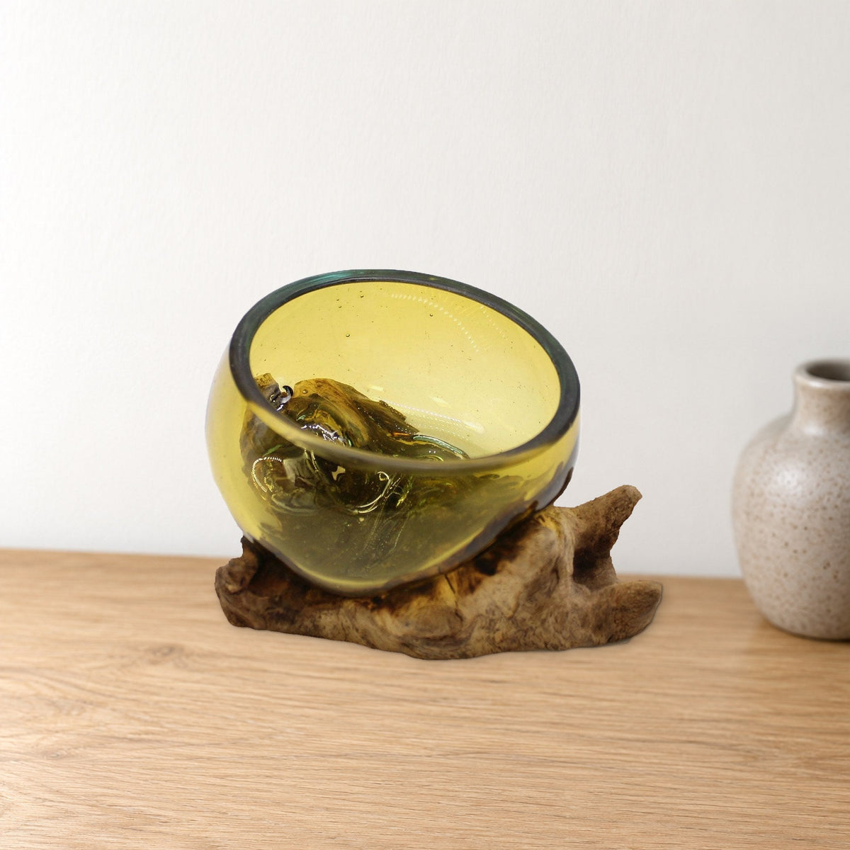 Mini amber molten glass bowl on gnarled wood, on a pale oak console beside a stoneware vase