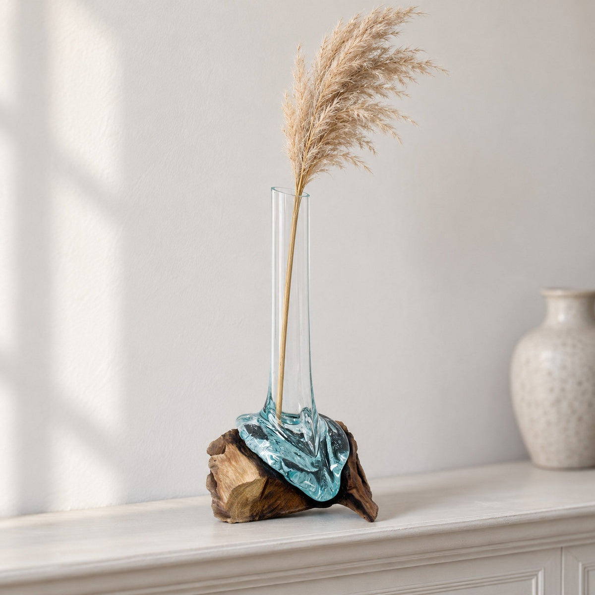 Tall molten glass vase on wood holding a dried pampas stem, on a painted mantelpiece