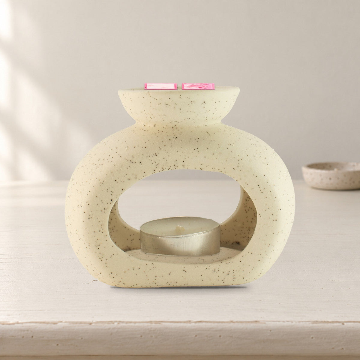 Speckled off-white pebble wax burner with Rose Quartz wax melt squares and an unlit tealight, on a painted dressing table