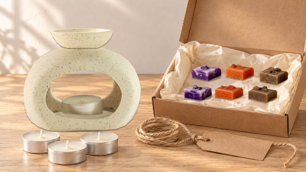 Speckled off-white pebble wax burner beside an open kraft gift box of purple, orange and brown crystal wax melt squares, with tealights, twine and a blank tag
