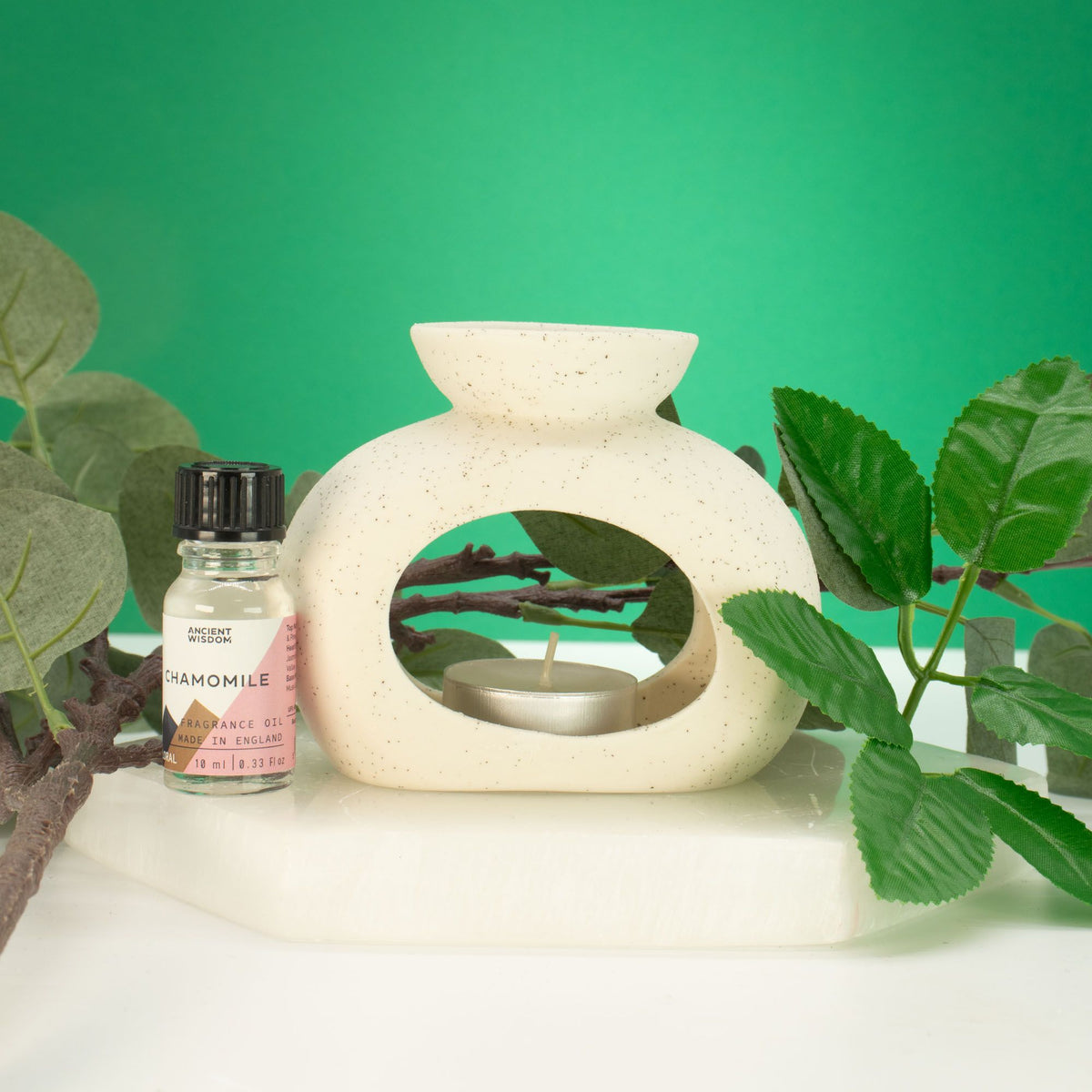 Pebble wax burner in speckled off-white ceramic with a tealight, styled with green leaves