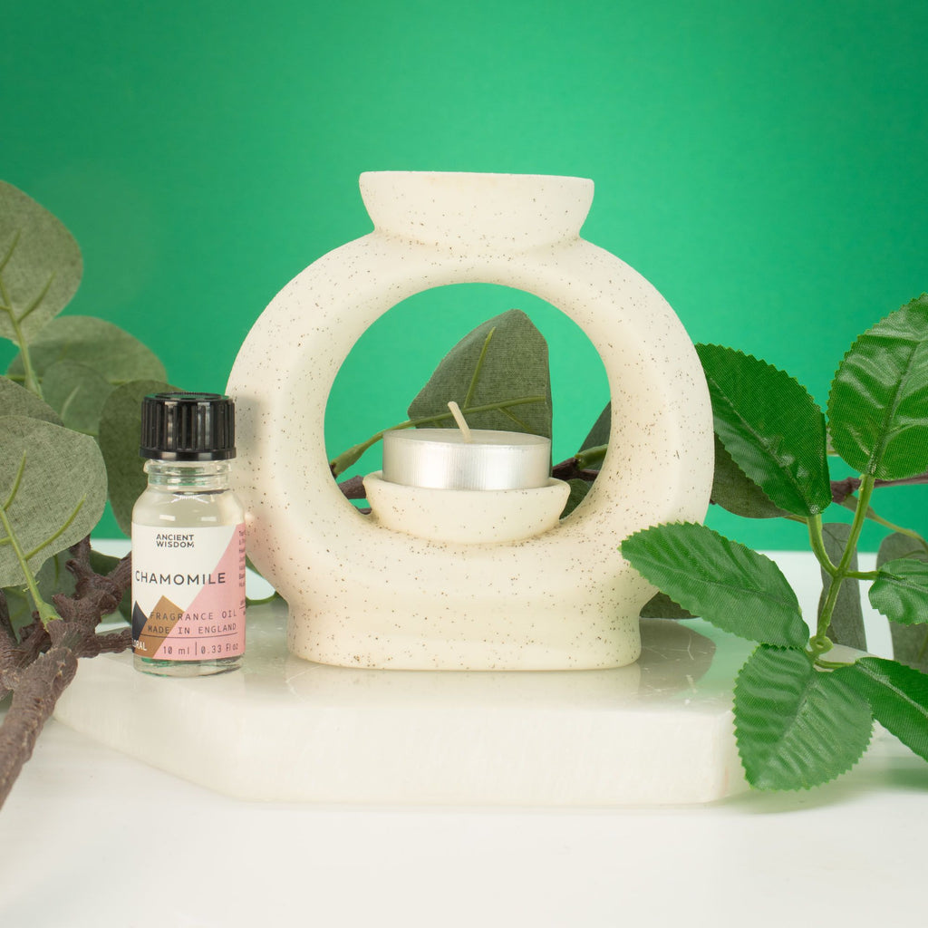 Large pebble wax burner in speckled off-white ceramic with a tealight, styled with green leaves