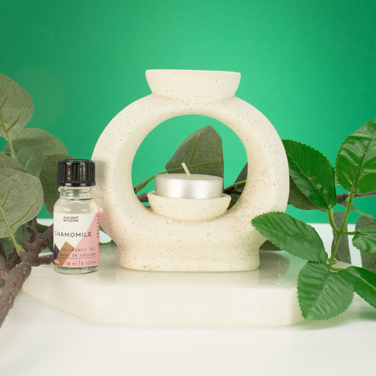 Large pebble wax burner in speckled off-white ceramic with a tealight, styled with green leaves