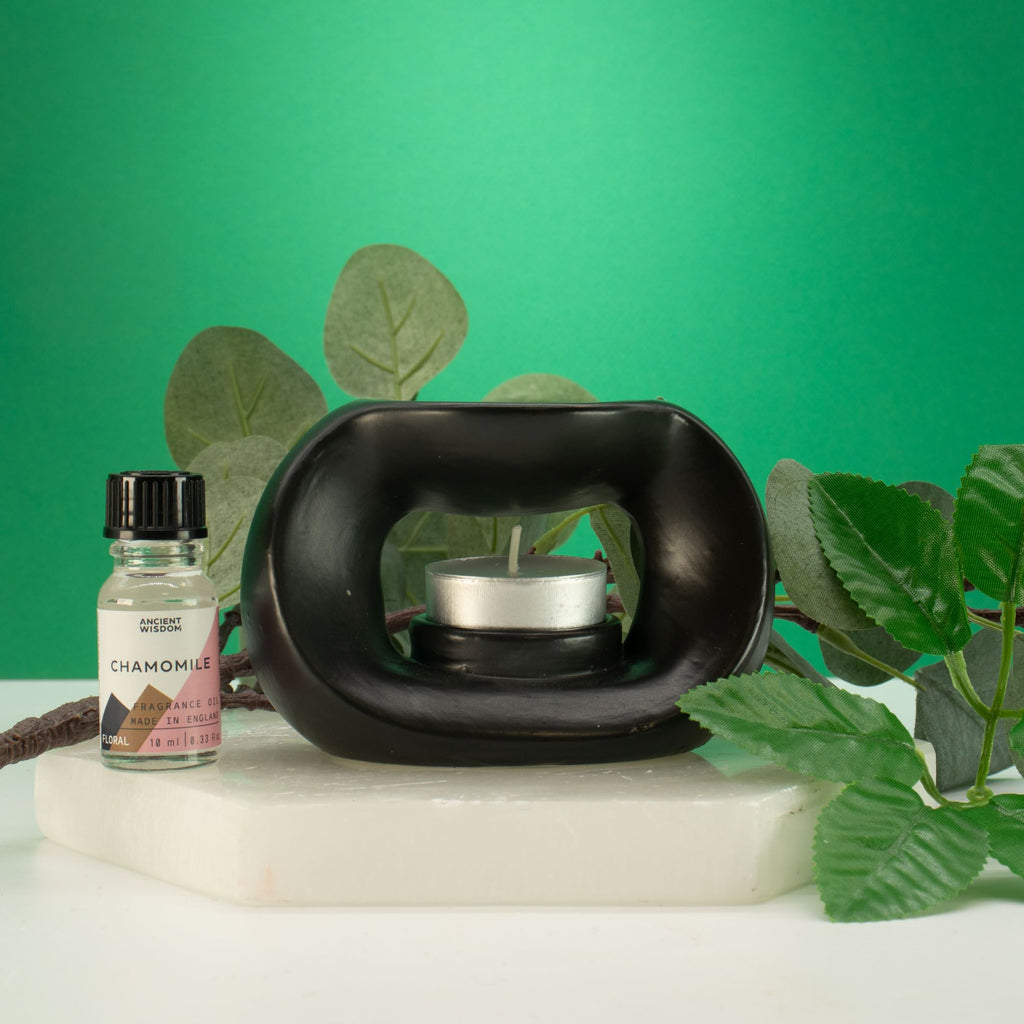 Matt black pebble wax burner with a tealight, styled with green leaves