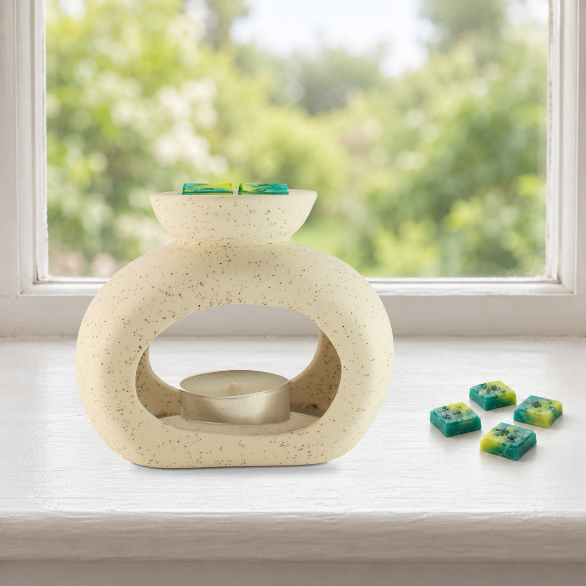 Speckled pebble wax burner with Emerald Forest green and yellow wax melt squares and an unlit tealight, on a painted windowsill