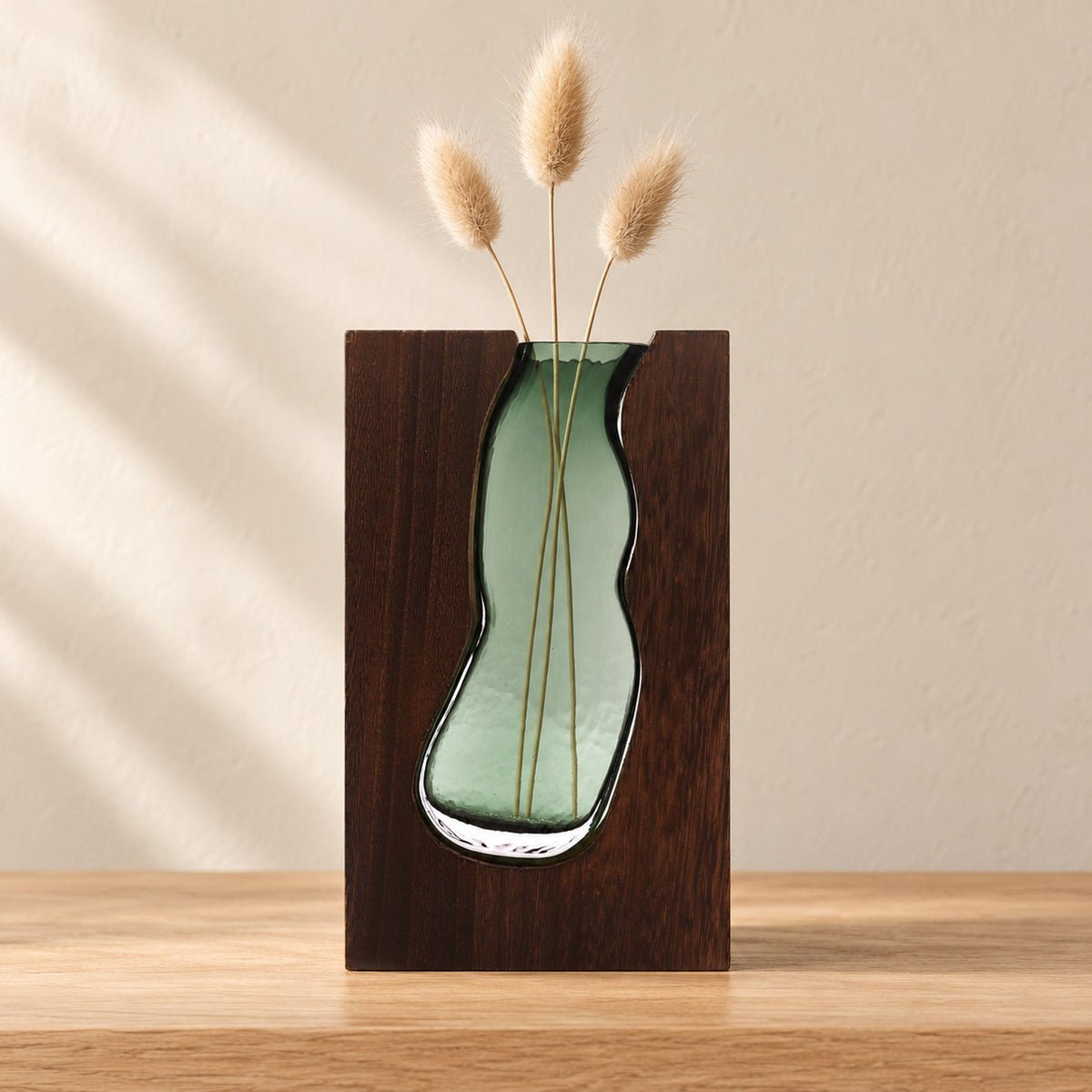 Green-tinted glass vase terrarium in dark tung wood holding three dried bunny-tail stems, on an oak console