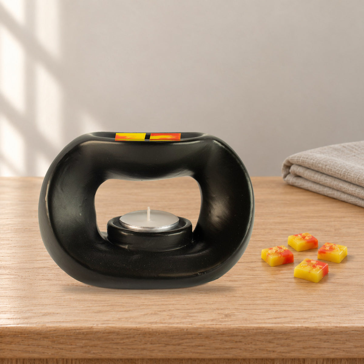 Matt black pebble wax burner with Golden Glow yellow and orange wax melt squares and an unlit tealight, on an oak coffee table