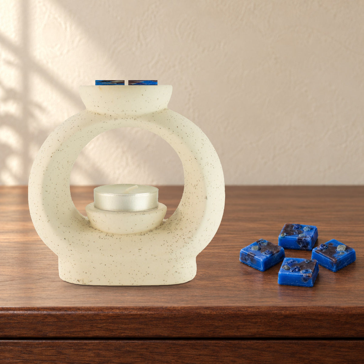 Large speckled pebble wax burner with Lapis Night royal blue wax melt squares and an unlit tealight, on a walnut sideboard