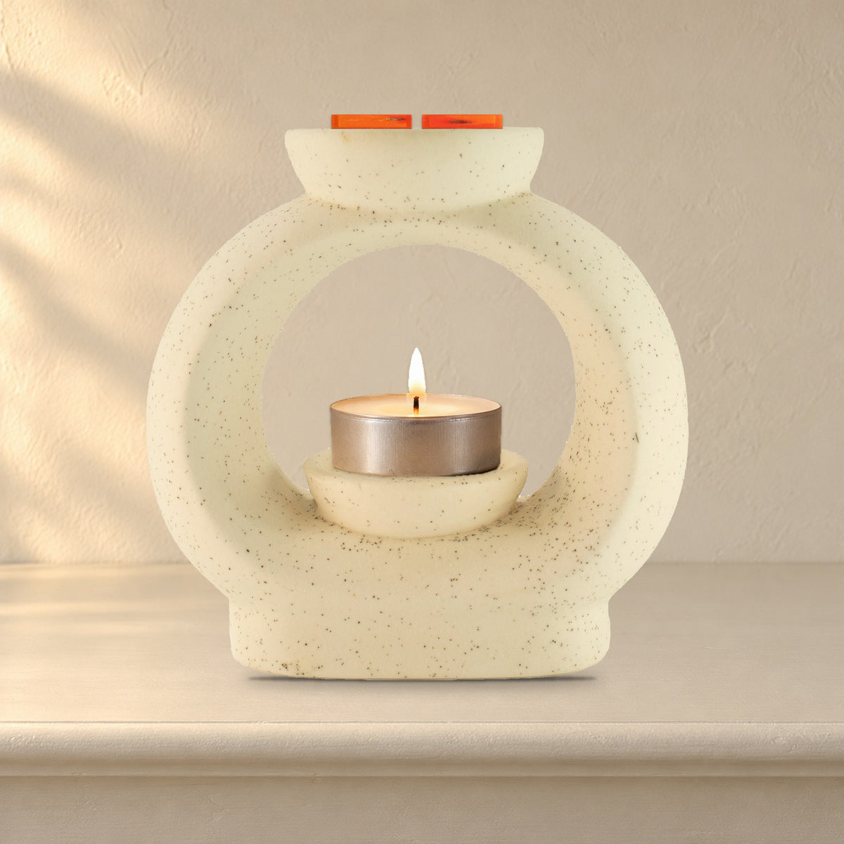 Large speckled off-white pebble wax burner with a lit tealight and Carnelian Fire wax melt squares, on a painted mantelpiece