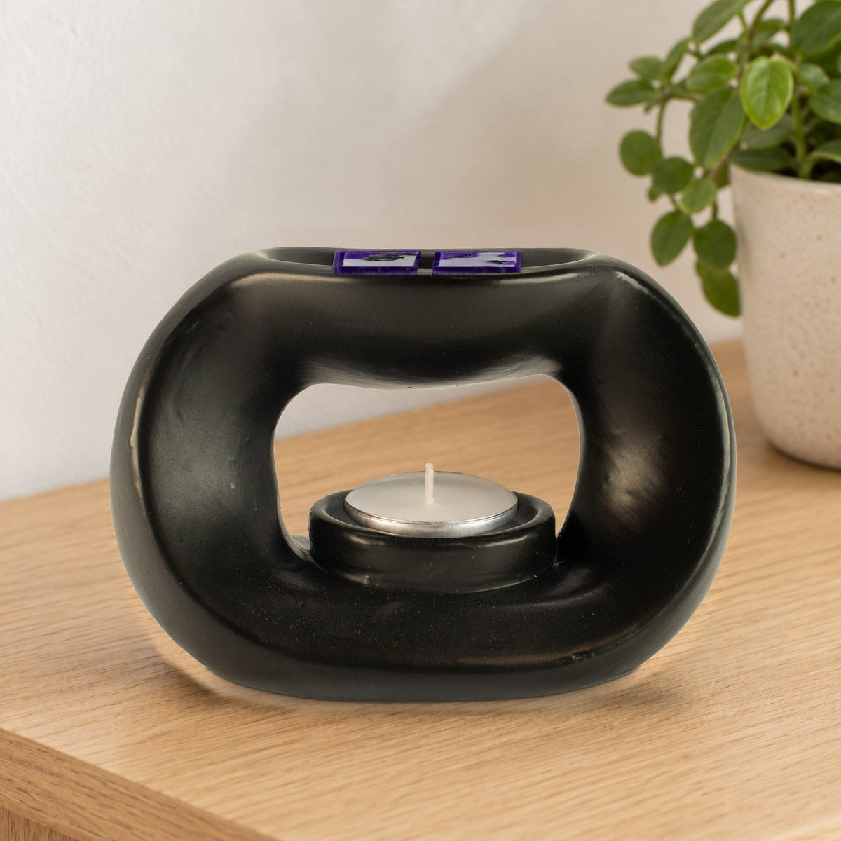 Two Amethyst Dream crystal wax melt squares in the dish of a matt black pebble wax burner, with an unlit tealight, on an oak side table