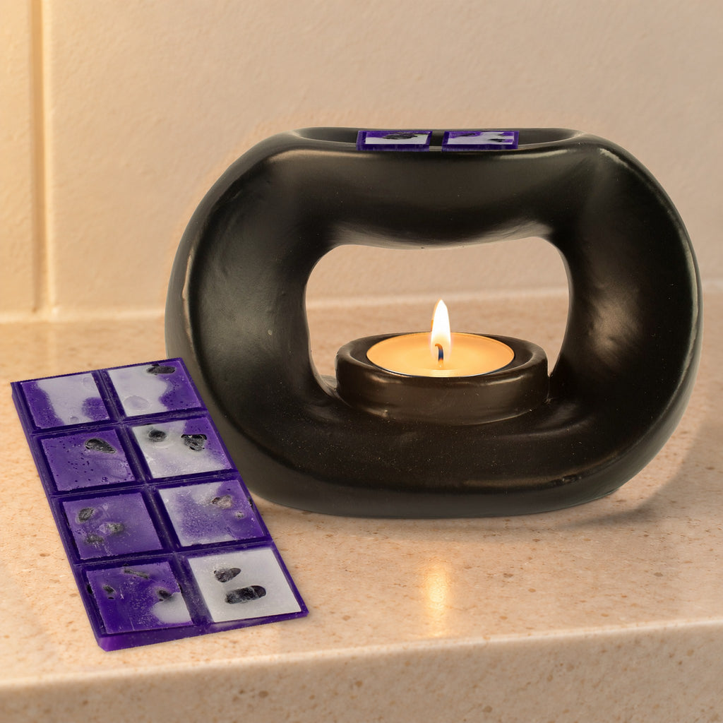 Matt black pebble wax burner with a lit tealight and Amethyst Dream wax melts, on a stone bathroom shelf