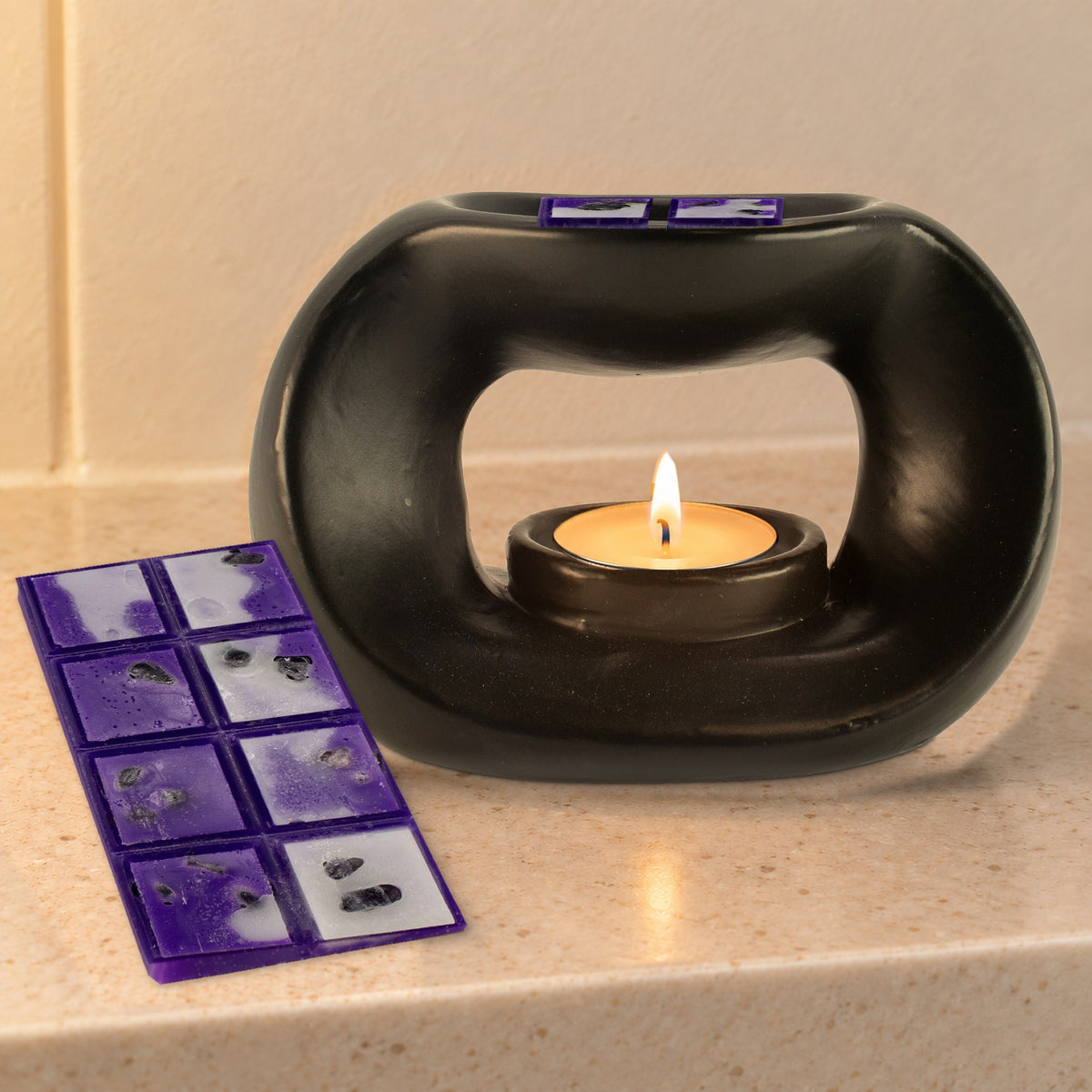 Matt black pebble wax burner with a lit tealight and Amethyst Dream wax melts, on a stone bathroom shelf