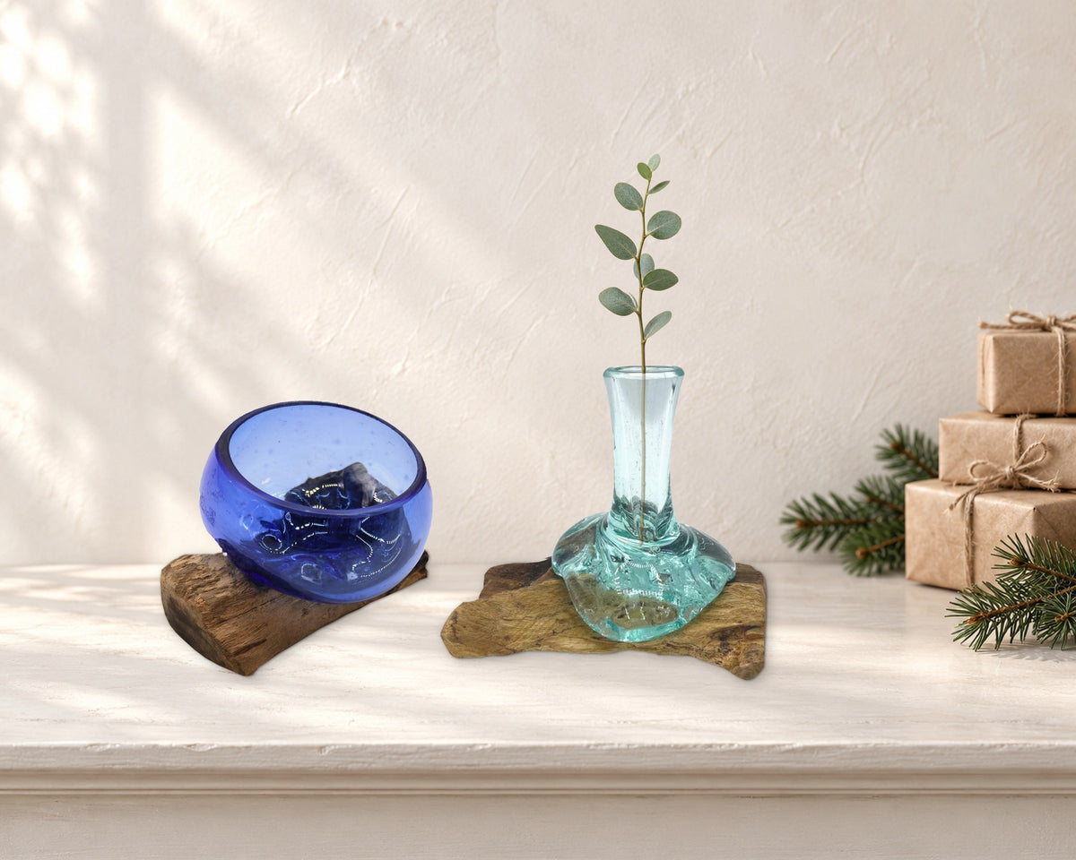 Mini cobalt blue molten glass bowl and small flower vase with a eucalyptus sprig, beside stacked kraft-wrapped gifts and pine on a mantelpiece
