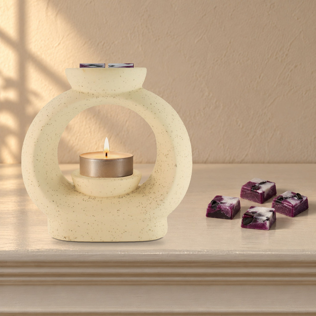 Large speckled pebble wax burner with a lit tealight and Obsidian Shield plum and white wax melt squares, on a painted mantelpiece
