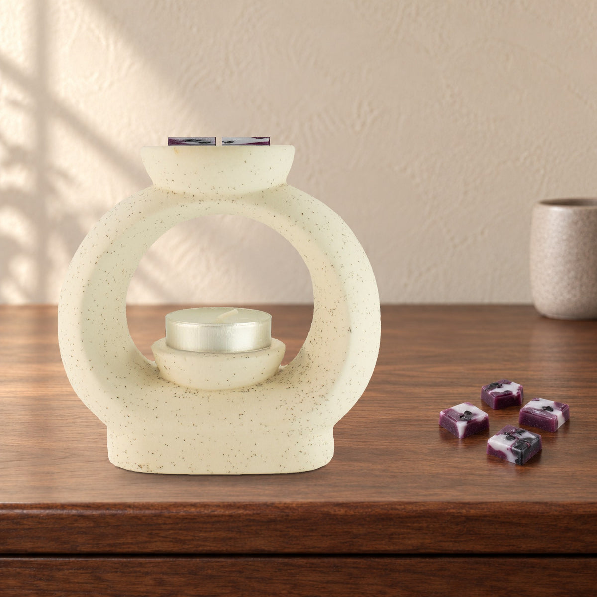 Large speckled pebble wax burner with Obsidian Shield plum and white wax melt squares and an unlit tealight, on a walnut shelf