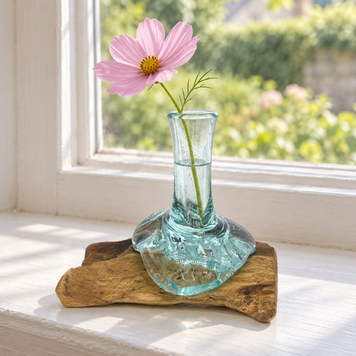 Small molten glass flower vase on wood holding a single pink cosmos, on a kitchen windowsill