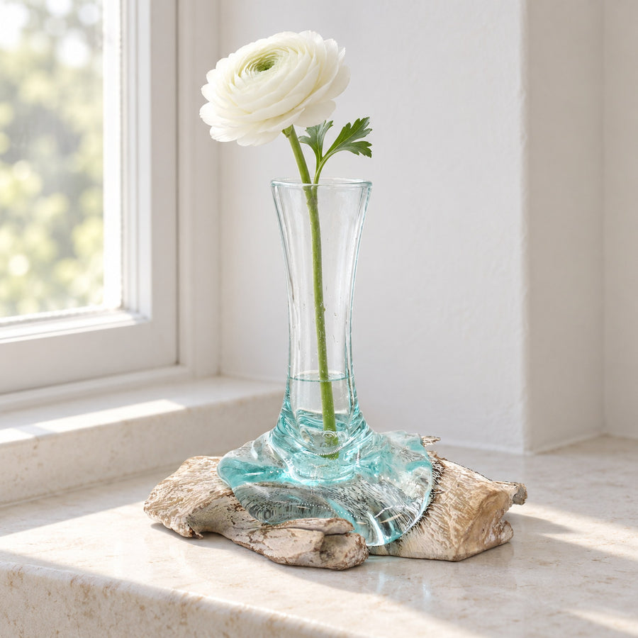 Small molten glass vase on whitewashed wood holding one white ranunculus, on a stone bathroom windowsill