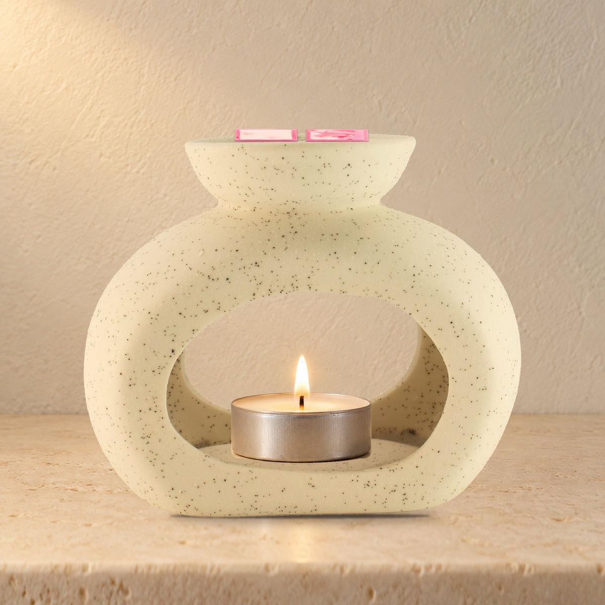 Speckled off-white pebble wax burner with a lit tealight and Rose Quartz wax melt squares, on a stone bathroom shelf