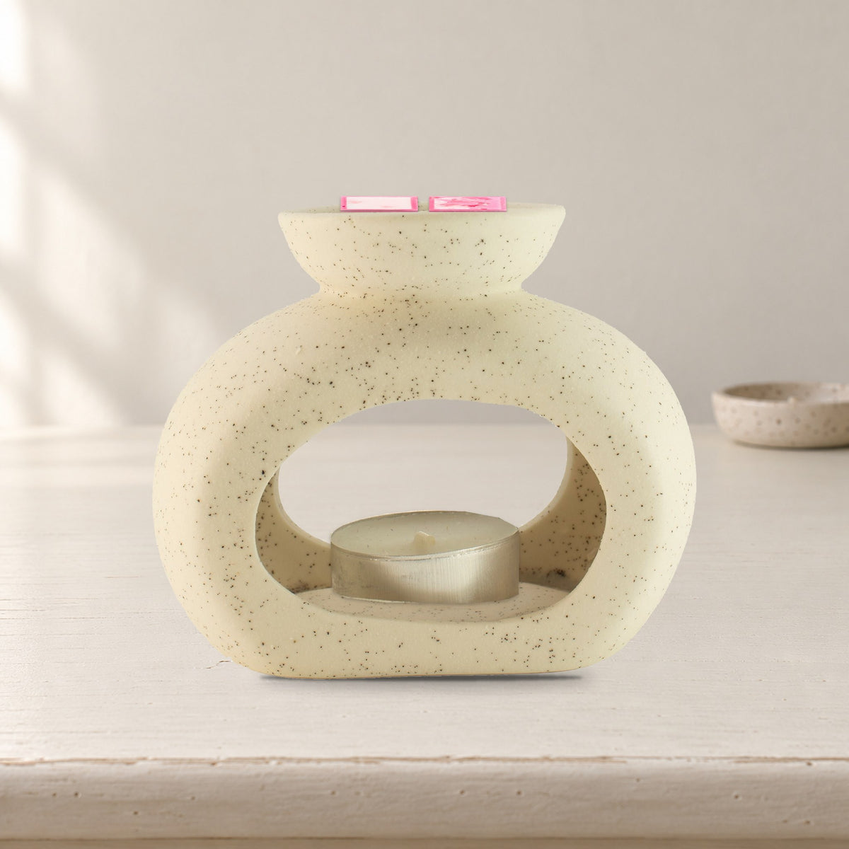 Speckled off-white pebble wax burner with Rose Quartz wax melt squares and an unlit tealight, on a painted dressing table