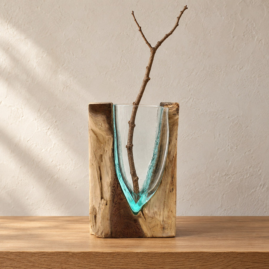 V-shaped molten glass vase in a block of wood holding a bare branch, on a console